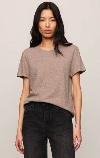 Woman wearing a brown t-shirt and dark jeans against a plain background