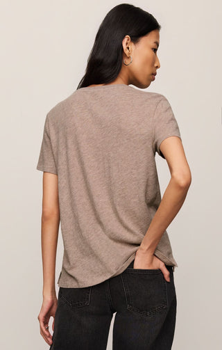 Woman wearing a beige t-shirt and black jeans against a plain background