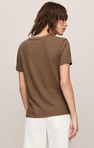 Woman wearing a brown t-shirt and white pants against a plain background