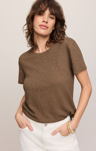 Woman wearing a brown t-shirt and white pants against a plain background