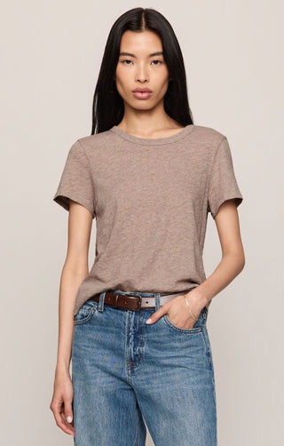 Woman wearing a brown t-shirt and blue jeans against a plain background
