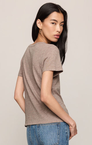 Woman wearing a brown t-shirt and blue jeans against a beige background