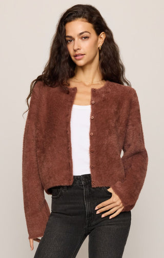 Woman wearing a brown cardigan over a white top and black pants on a beige background