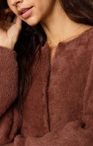 Close-up of a woman wearing a soft, fuzzy brown cardigan or sweater with a round button closure and a delicate gold necklace.