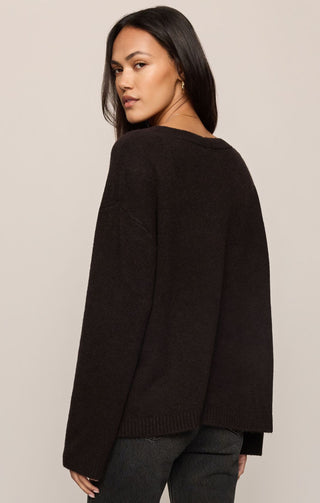 A woman wearing a dark brown knit sweater, shown from a side-back angle against a solid light beige background.