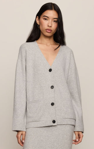 Woman wearing a gray cardigan with black buttons on a beige background