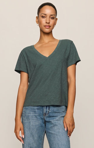 Woman wearing a green t-shirt and blue jeans against a beige background