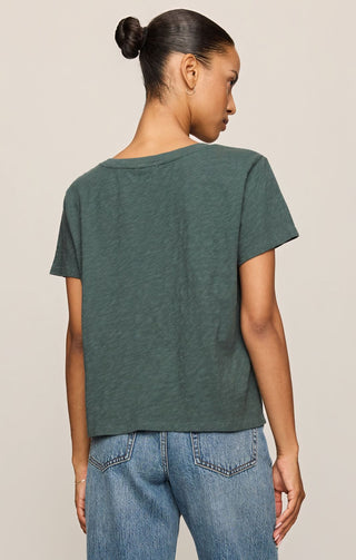 Person wearing a green t-shirt and blue jeans on a beige background