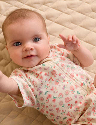 Baby wearing a floral outfit on a beige quilted surface