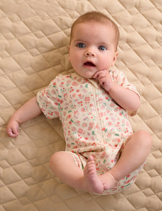Baby wearing a floral onesie on a quilted surface
