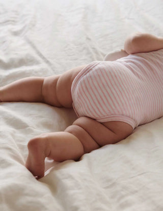 Baby in pink striped onesie lying on a white blanket