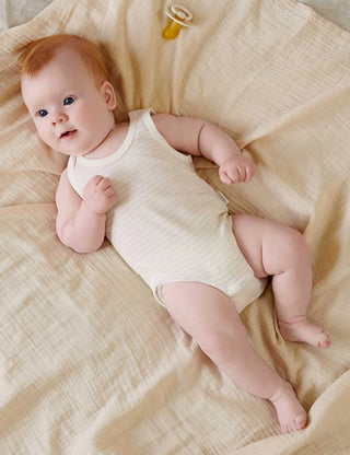 Baby in a white onesie lying on a beige blanket