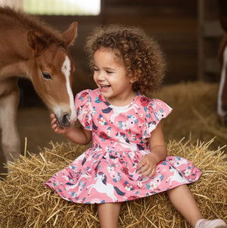 Child in a pink dress with horse print sitting on hay next to a horse