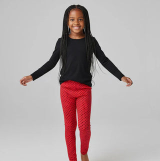 Child wearing a black long-sleeve top and red polka dot leggings on a gray background