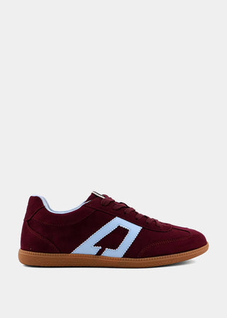 A low-top suede sneaker in burgundy with a light blue geometric side stripe, a white stitched border, and a brown gum sole, shown against a plain light gray background.
