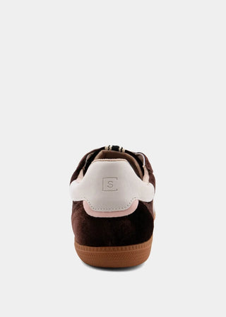 A single low-top sneaker shown from the rear, featuring dark brown suede and white leather panels with a light pink accent stripe and a gum brown sole, on a light gray background.