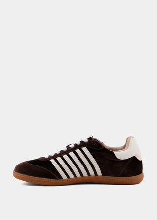 A dark brown suede sneaker with three white stripes on the side, white laces, a white heel tab, and a gum brown sole, shown in profile against a light gray background.
