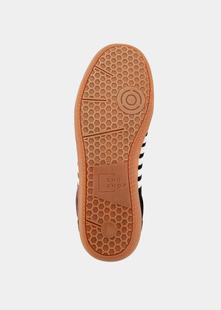 A top-down view of a shoe's brown gum rubber sole, showing a honeycomb tread pattern and the embossed brand name 'SHU SHU SHU'.