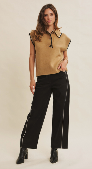 Woman wearing a beige top with black trim and black pants with white stripes on a beige background