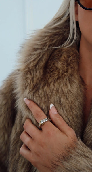 Close-up of a person wearing a fur coat with a hand touching the fabric, wearing a gold ring.