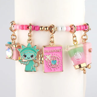 A beaded charm bracelet displayed on a white cylindrical stand. The bracelet features pink and white beads with gold-tone hardware and four dangling charms: a pink camera, a mint green cartoon character, a pink passport, and a pink cup with a strawberry.
