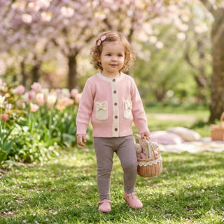 Young girl in a pink cardigan standing in a garden with cherry blossoms and tulips.