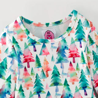 A close-up of a white long-sleeve top featuring an all-over watercolor pine tree pattern in shades of teal, green, pink, and orange. A small pink barn graphic is visible on the inner neck label.