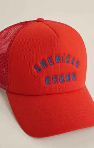 Red trucker hat with 'American Grown' text on a beige background