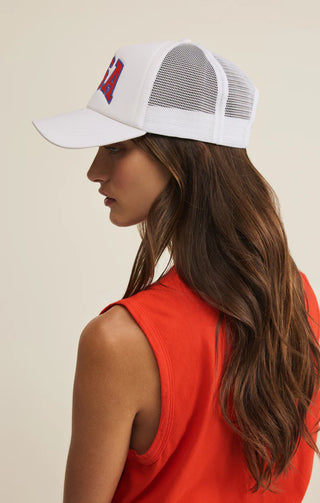 Woman wearing a white trucker cap with a red and blue logo on a beige background