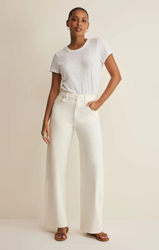Woman wearing a white t-shirt and cream-colored wide-leg pants on a beige background