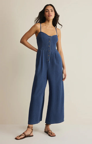 Woman wearing a blue denim jumpsuit on a beige background