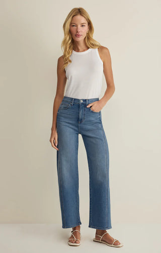 Woman wearing a white sleeveless top and blue jeans on a beige background