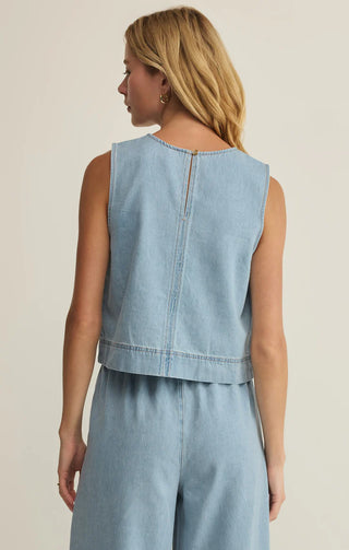 Woman wearing a light blue denim sleeveless top and pants on a beige background
