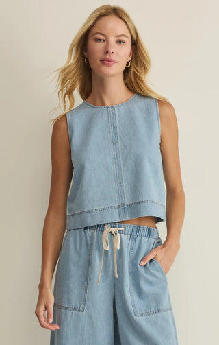 Woman wearing a light blue sleeveless top and wide-leg pants against a beige background
