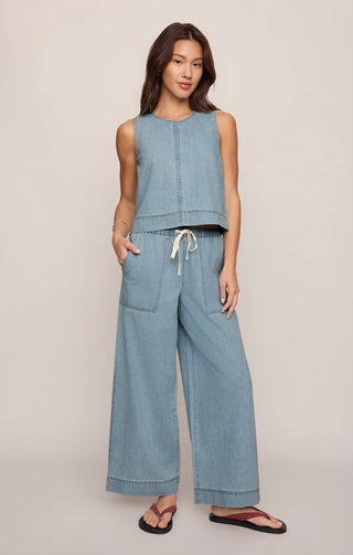 Woman wearing a light blue sleeveless top and wide-leg pants on a beige background