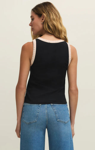 Woman wearing a black tank top with lace trim and blue jeans on a plain background