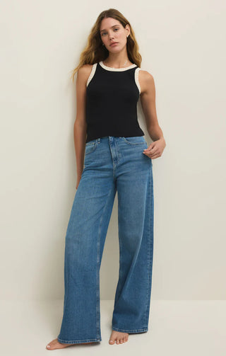 Woman wearing a black sleeveless top and blue jeans against a plain background
