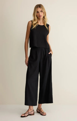 Woman wearing a black sleeveless top and wide-leg pants on a beige background