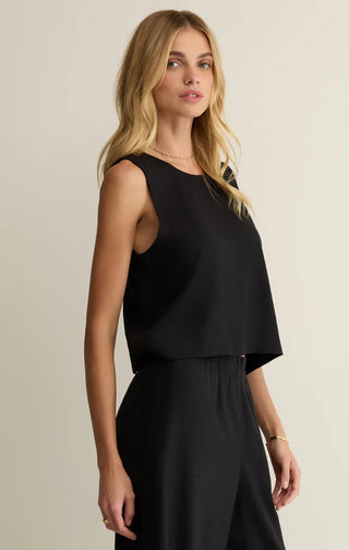 Woman wearing a black sleeveless top and black pants against a beige background
