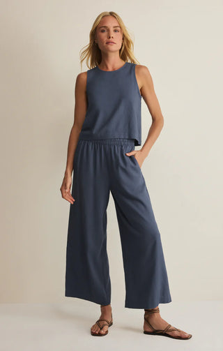 Woman wearing a sleeveless navy top and wide-leg pants on a beige background