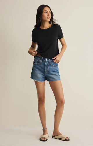 Woman wearing a black t-shirt and denim shorts on a beige background
