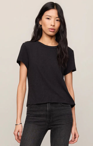 Woman wearing a black t-shirt and dark jeans against a plain background