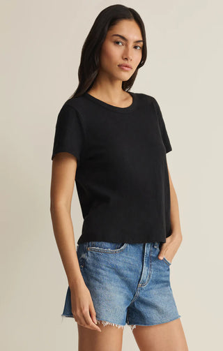 Woman wearing a black t-shirt and denim shorts on a beige background