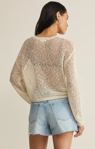Woman wearing a beige knit sweater and denim shorts on a plain background