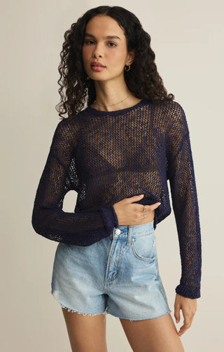 Woman wearing a dark blue mesh sweater and light blue shorts on a beige background