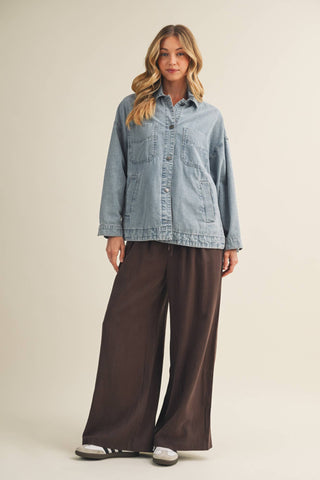 Woman wearing a light blue denim jacket and brown wide-leg pants on a beige background