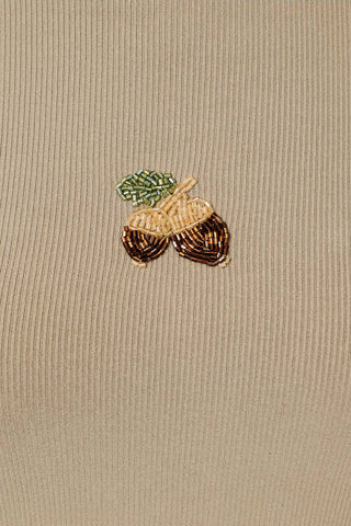 A close-up of a beige ribbed knit fabric featuring a small embroidered acorn motif in brown, gold, and green thread.