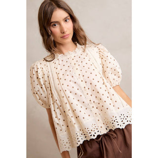 Woman wearing a beige blouse with lace details against a neutral background