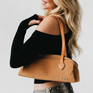 Woman holding a brown handbag against a plain background