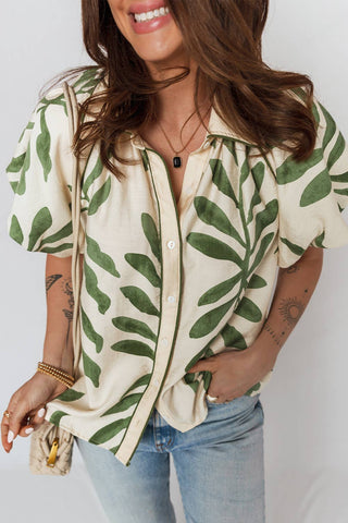 Woman wearing a beige blouse with green leaf pattern and blue jeans against a white background
